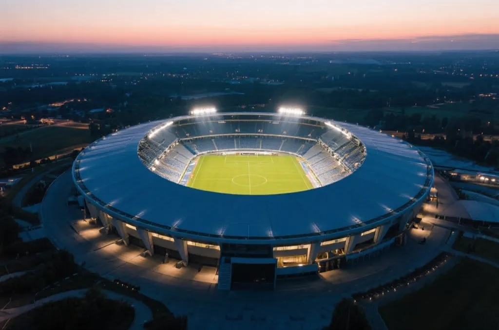 An aerial view of a modern, majestic sports stadium at dusk, with soft stadium lights turning on, no logos or text visible